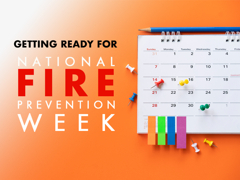 A calendar with colorful push pins on an orange background, next to text that reads "Getting Ready for National Fire Prevention Week.