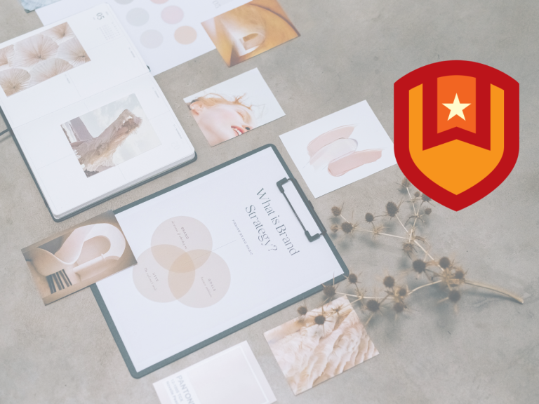 A flat lay of design materials, including photos, color swatches, and a strategy diagram, arranged on a gray surface with dried plants. A bold red and orange shield emblem with a star appears in the upper right corner.