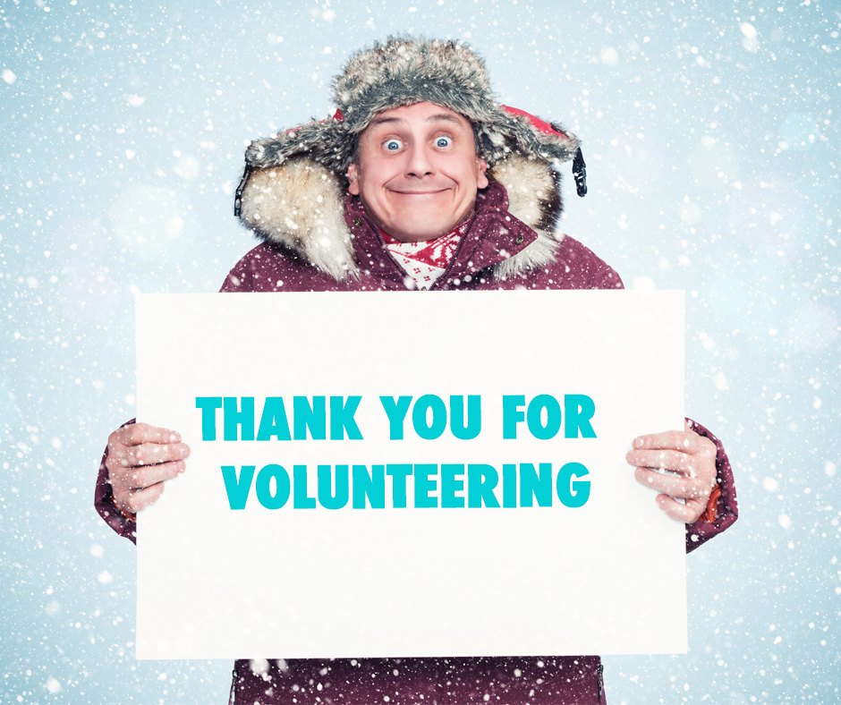 A smiling person in a winter coat and furry hat holds a sign reading "Thank you for volunteering" in bold turquoise letters, with snow falling around them.
