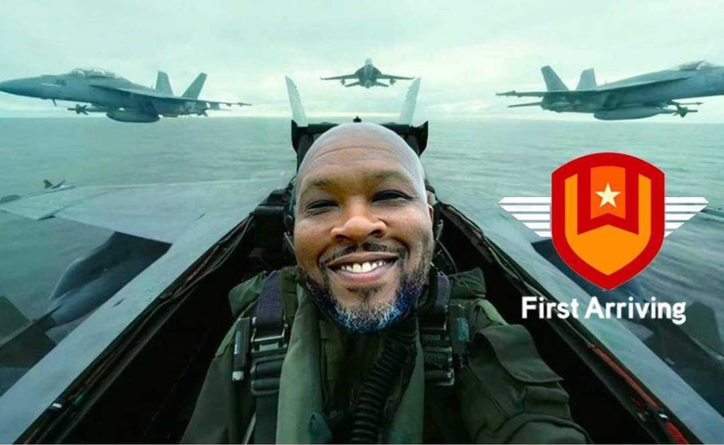 A smiling man is photoshopped into the cockpit of a fighter jet, with three jets flying over water behind him. A red and yellow shield logo and the text "First Arriving" appear in the lower right corner.