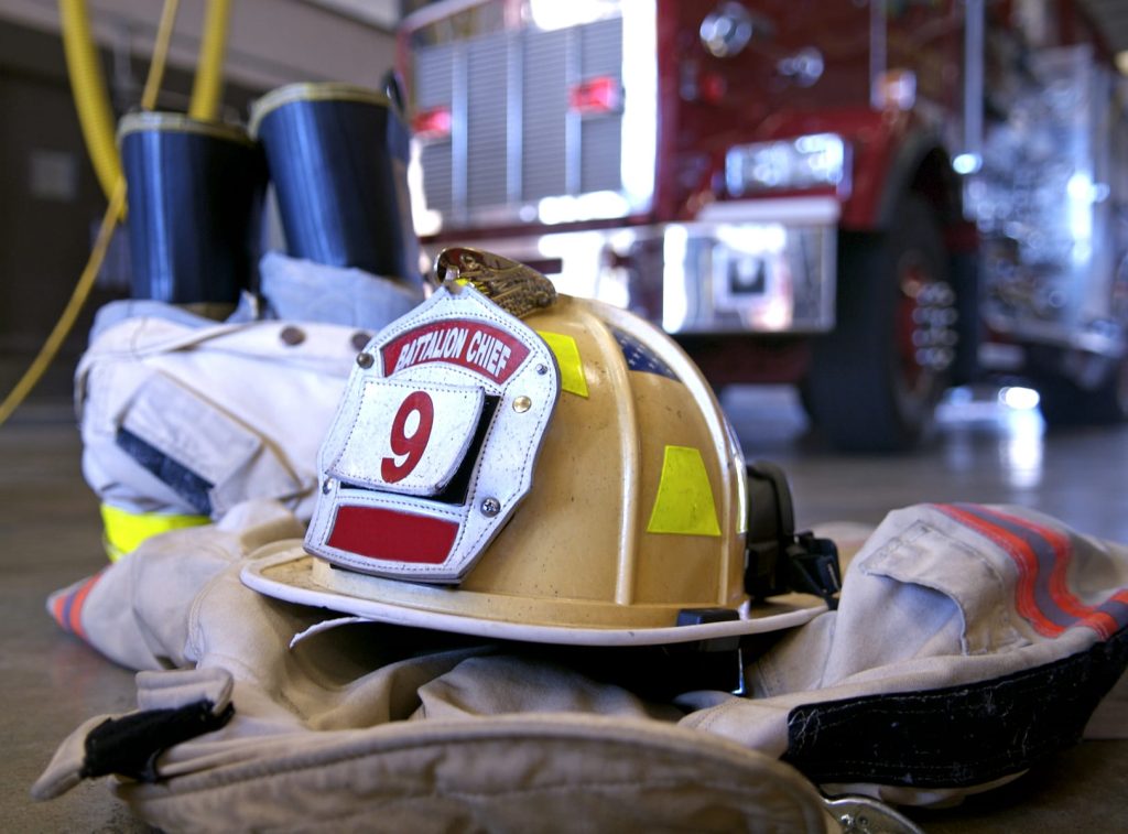 A fire chief’s helmet labeled “9” and protective gear rest on the floor in front of a red fire truck inside a fire station.