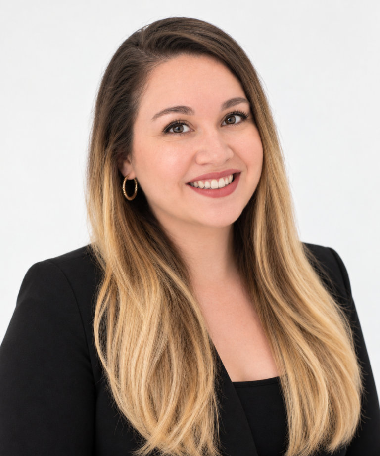 A woman with long, straight, blonde hair wearing a black blazer and gold hoop earrings smiles at the camera against a plain white background.
